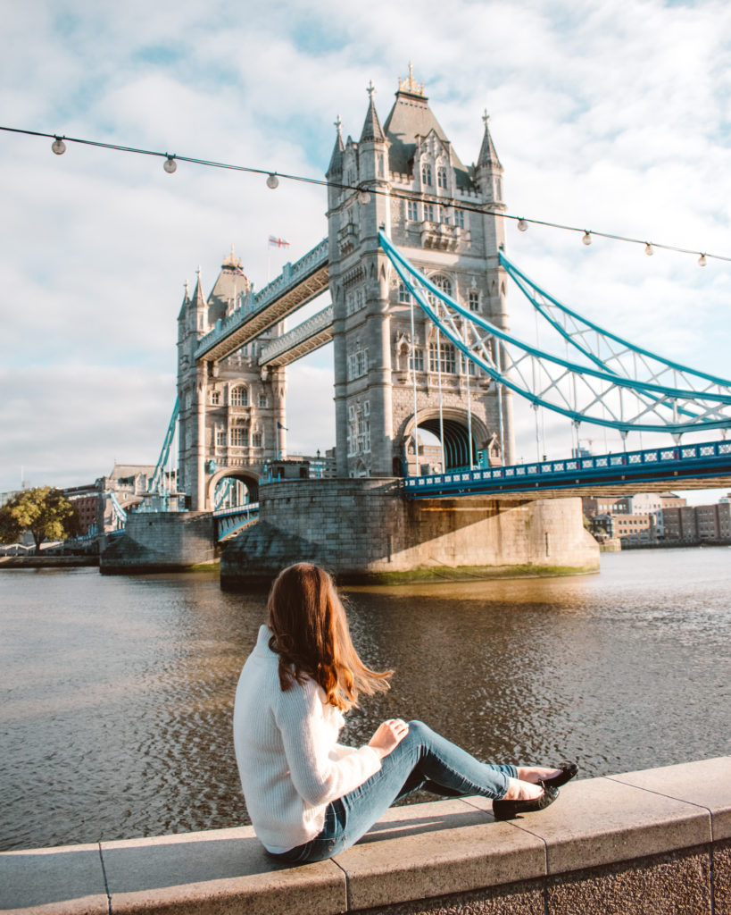 Woman sat on a wall in front of Tower Bridge in early morning sun