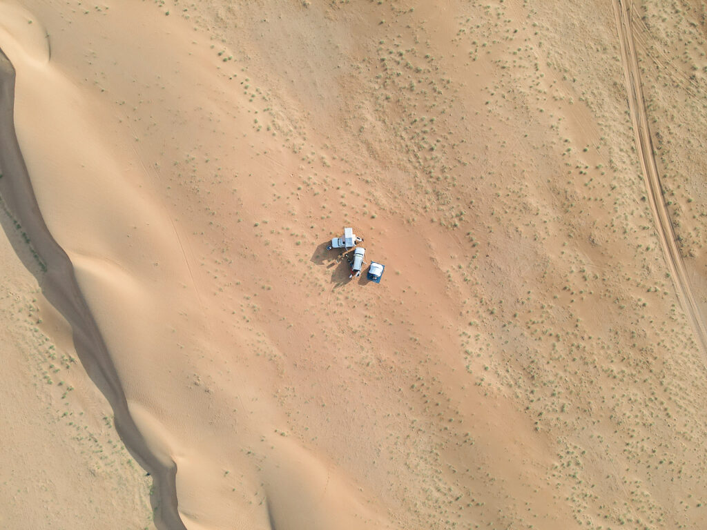 High up aerial photo of two cars and a tent in the desert of Oman