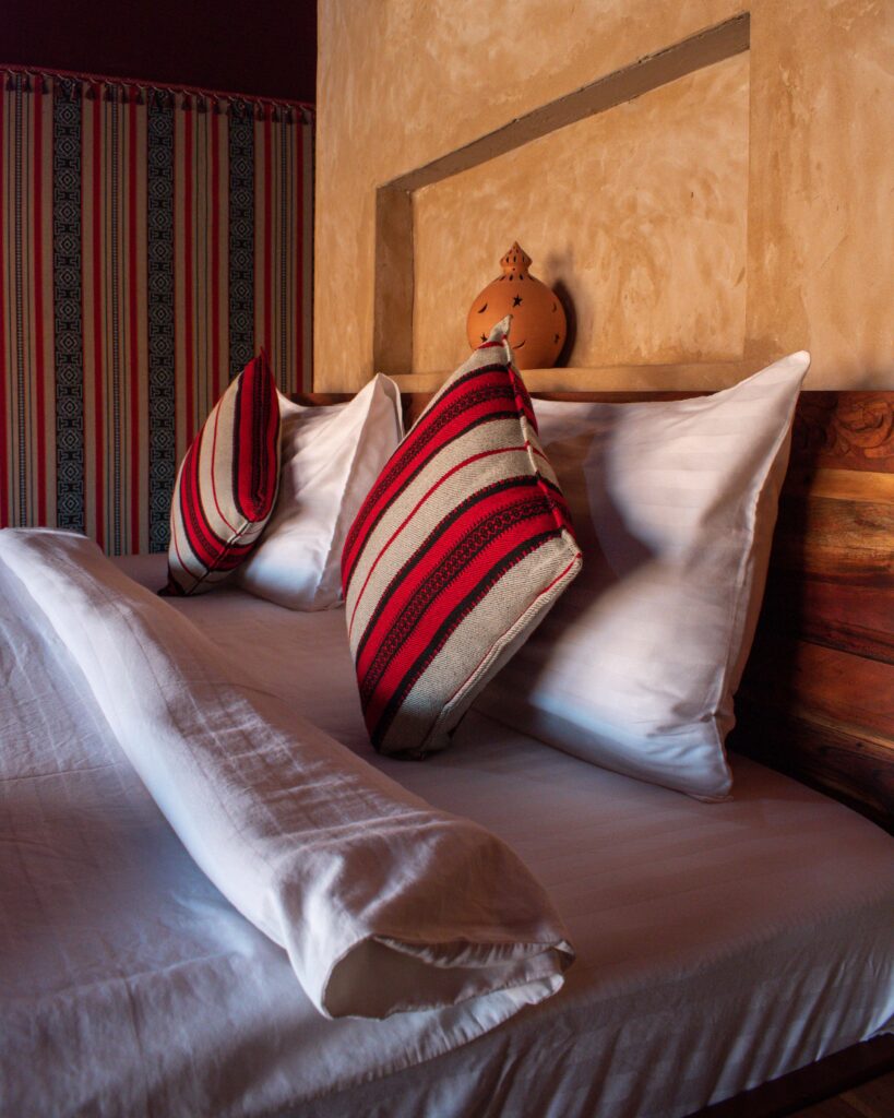 Close up of bed covered with white duvet and red and cream striped cushions against a terracotta coloured wall
