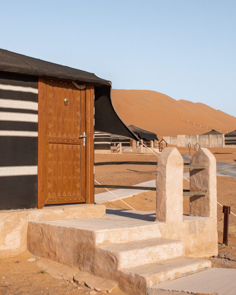 Fixed black and white stripped tent in the Omani desert, with brown wooden door and terracotta stone steps