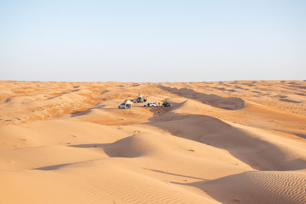 Three cars parked in amongst golden sand dunes in Wahiba Sands, Oman