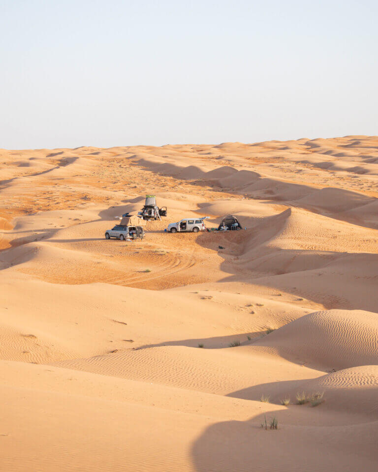Three cars parked in amongst golden sand dunes in Wahiba Sands, Oman
