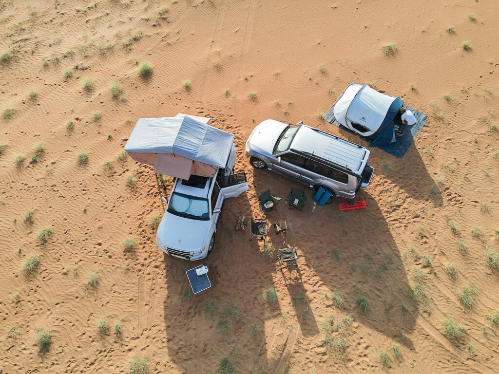 Aerial photo of two white cars and a tent parked around camp chairs in Wahiba Sands, Oman