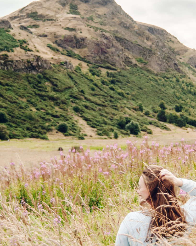 Woman sat in long grass in front of Arthur's Seat