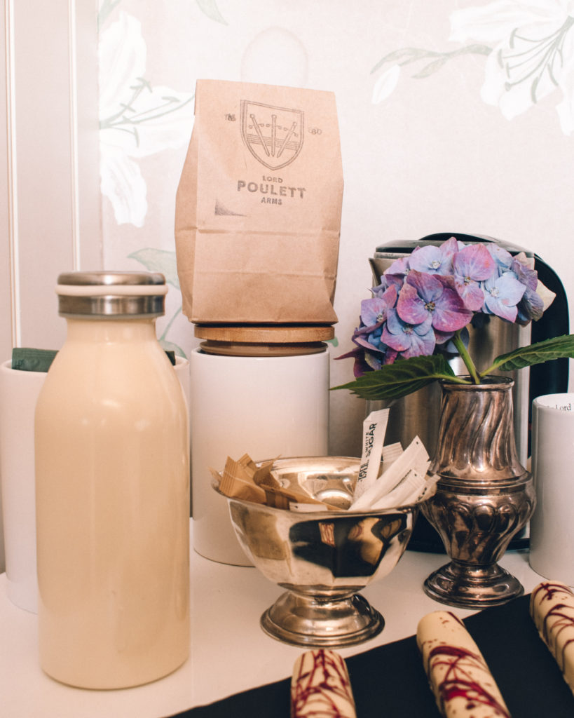 Long white chocolates in front of purple sweet peas in a silver jug