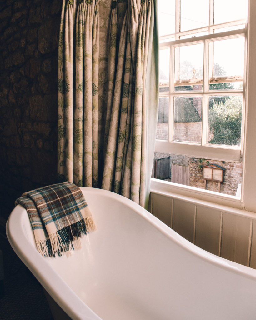 Roll top bath in front of a sash window, with tartan curtains and a tartan blanket