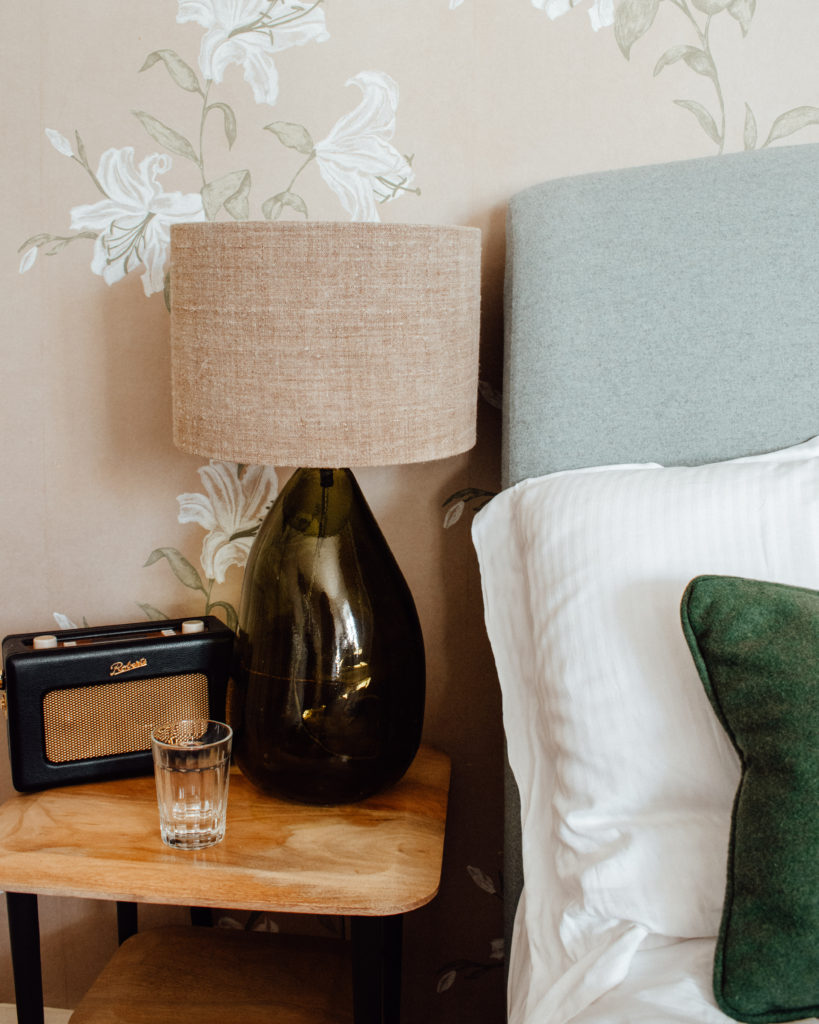 Bedside table with glass lamp and retro radio in front of pastel floral wallpaper