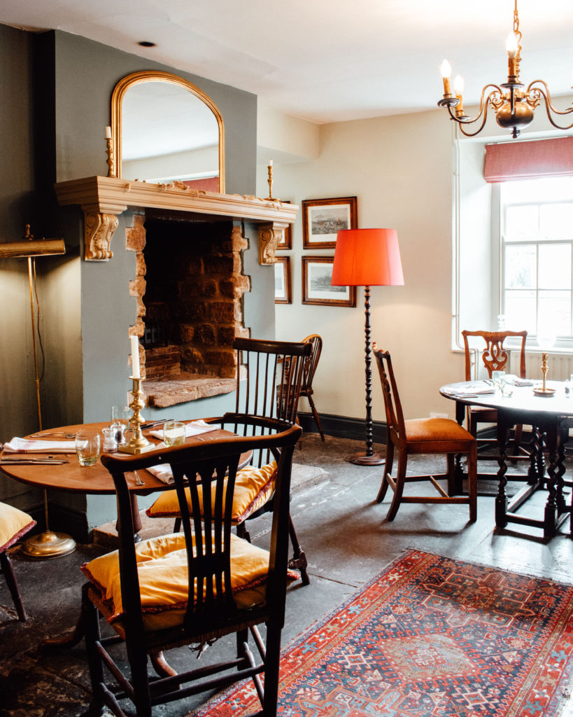 Pub dining room with wooden tables, red woven carpets, and a fireplace