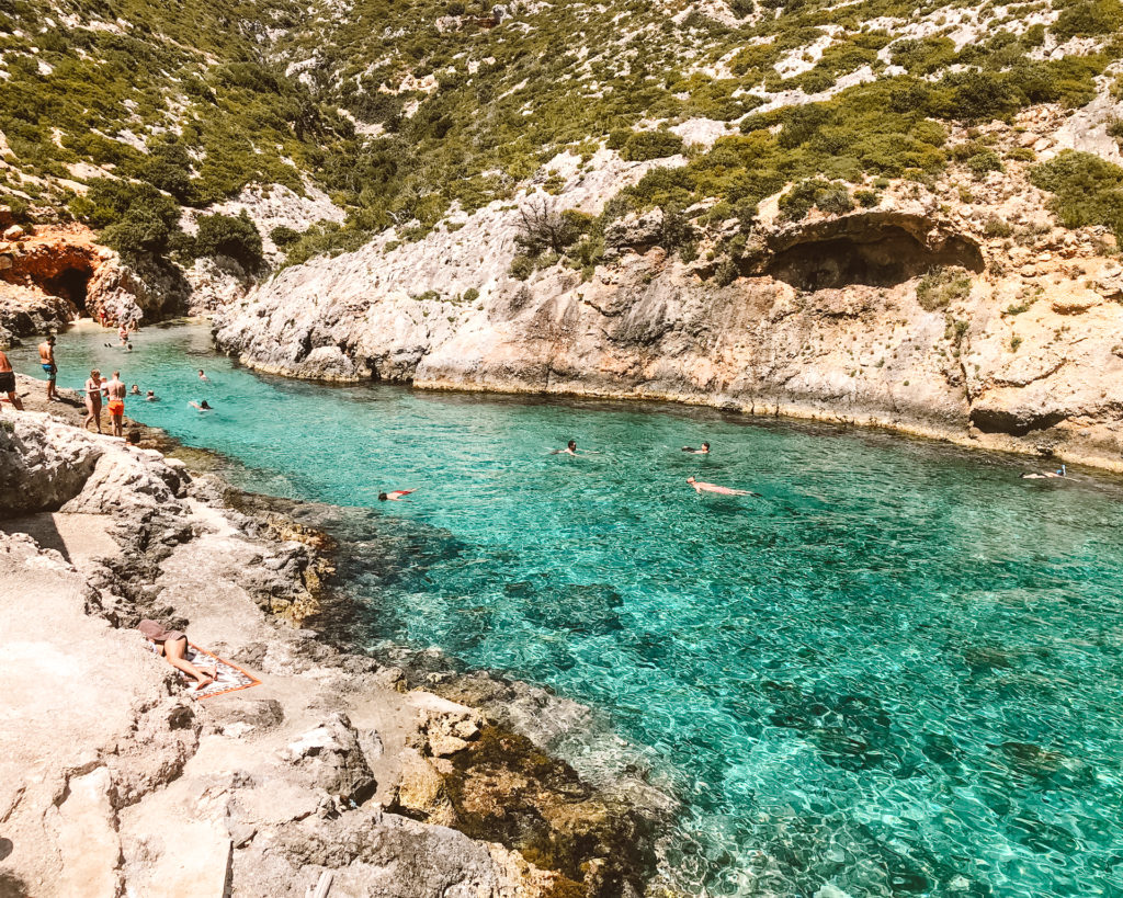 People swimming in crystal clear, turquoise water in cove on Zakynthos