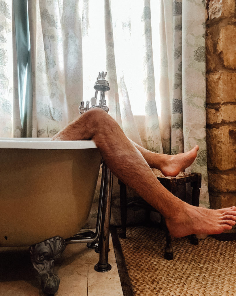 Man's legs dangling over edge of bath in front of a window