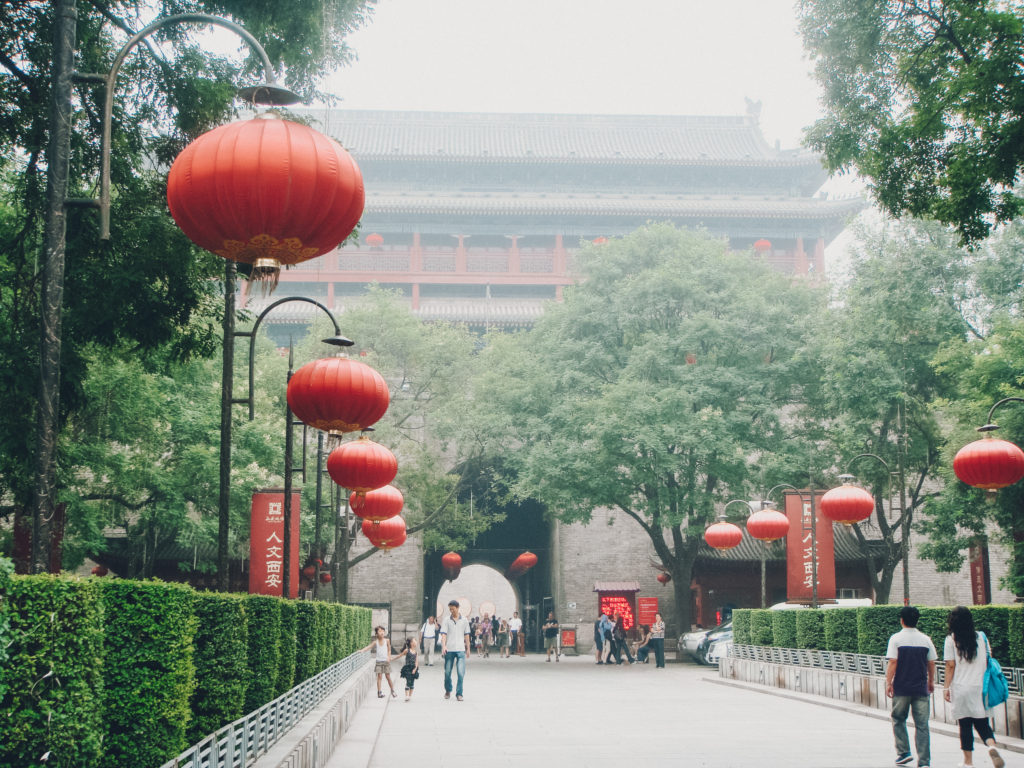 People walking along tree lined avenue with hanging red lanterns in Xi'An