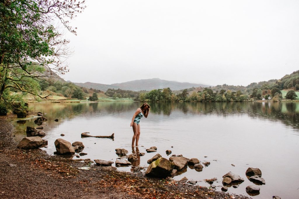 Woman in blue swimsuit wading into Rydal Water, Lake District, in the rain