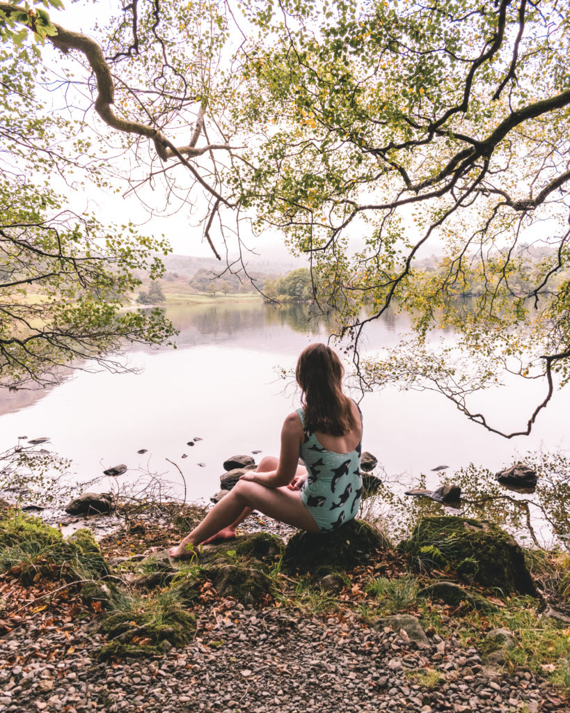 Woman in blue swimming costume sat at the edge of Rydal Water, Lake District