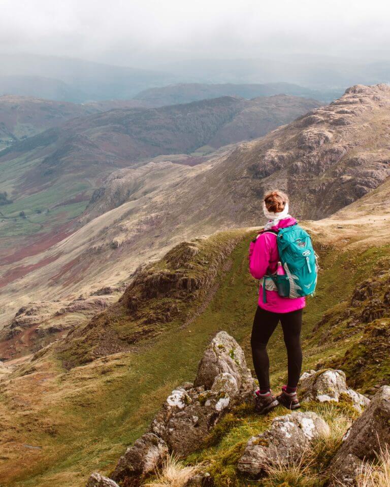 Woman in pink waterproof jacket looking out from the top of Crinkle Crag ridge