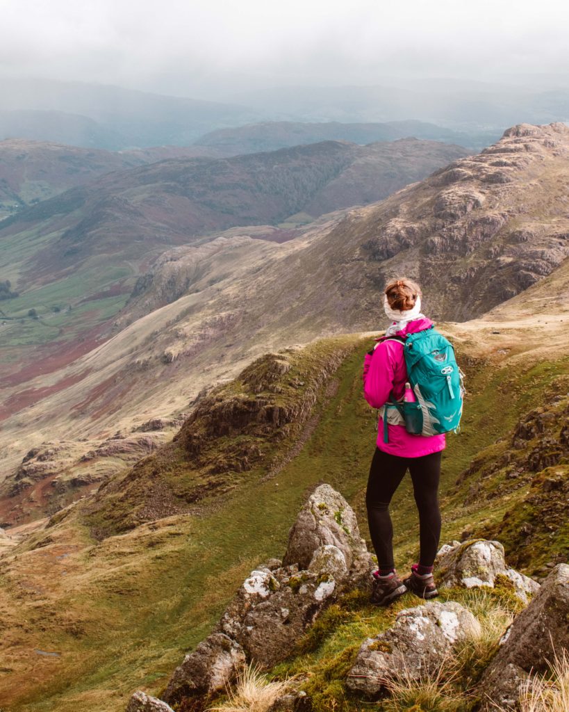Woman in pink waterproof jacket looking out from the top of Crinkle Crag ridge