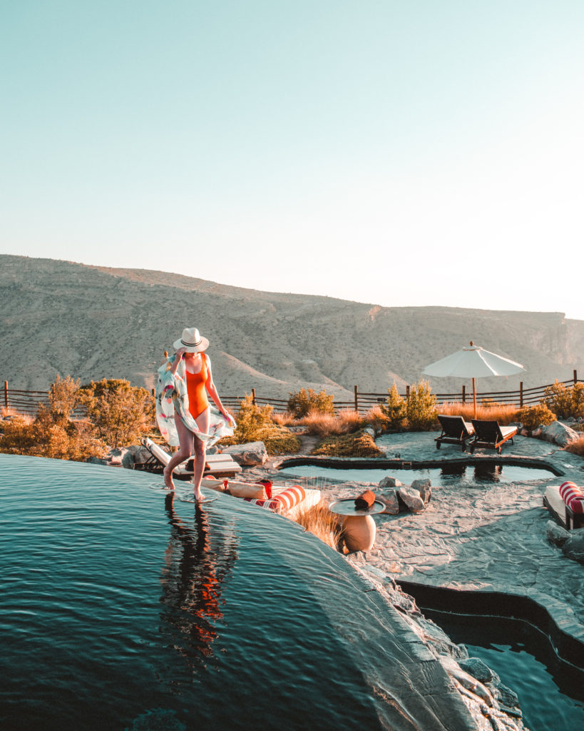 Woman walking along edge of infinity pool in orange swimsuit