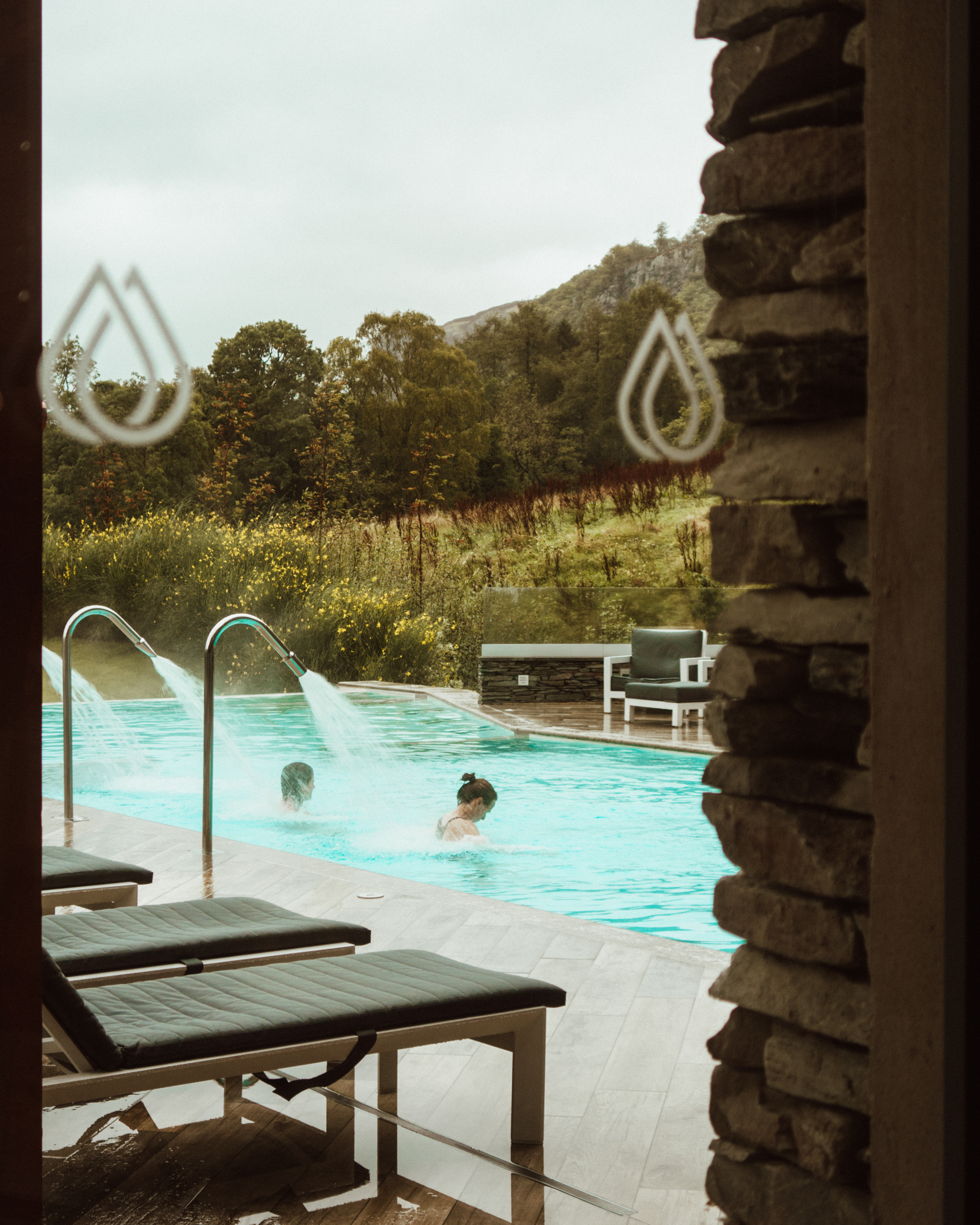 Two women in the blue swimming pool at Lodore Falls spa on a wet day