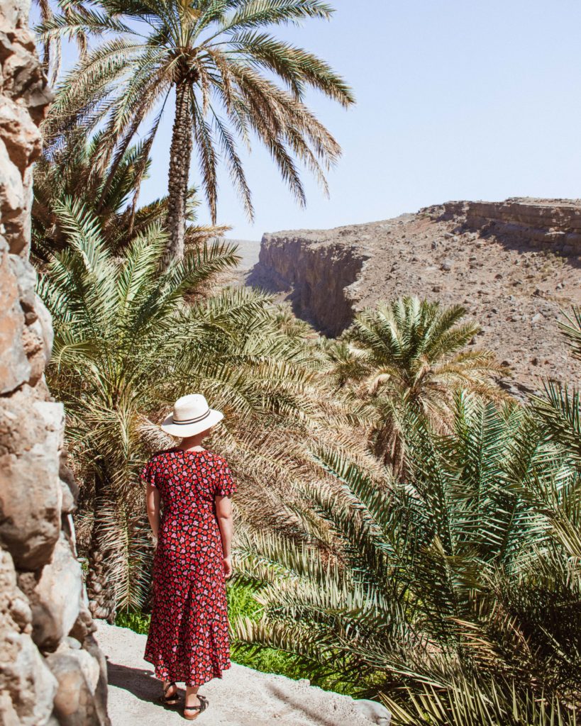 Woman in red dress walking though palm trees at Misfat Al Abriyeen