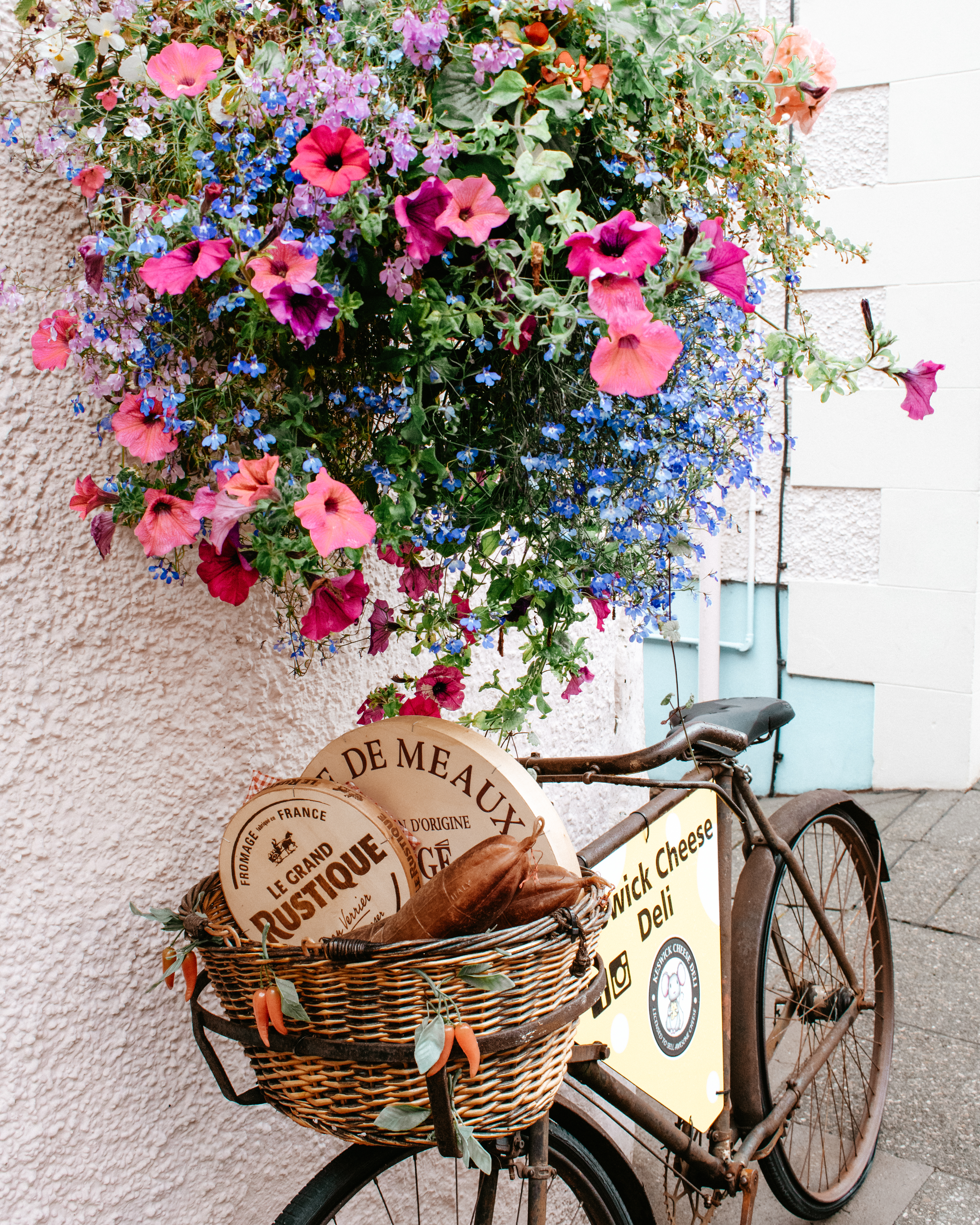 Large flower basket above a bike filled with cheeses outside the Keswick Cheese company