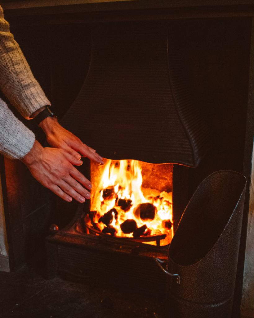 Man warming his hands over a fire in the Traveller's Rest on a rainy day in the Lake District