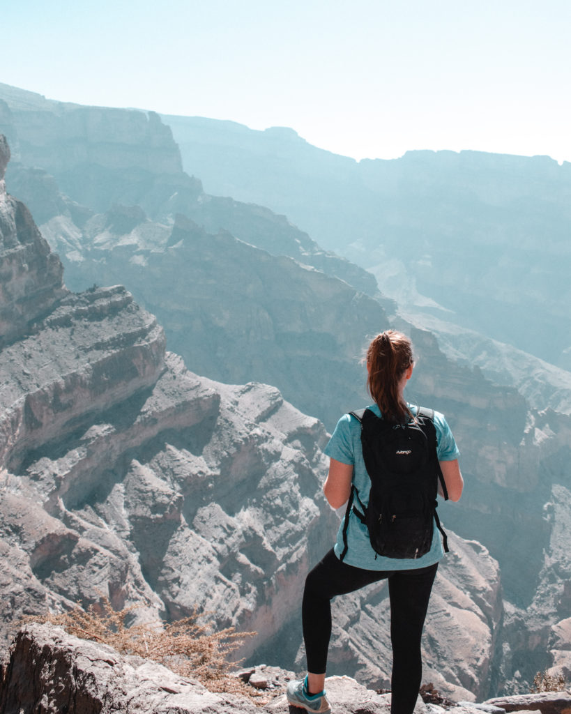 Woman in blue top and black rucksack looking into Wadi Ghul