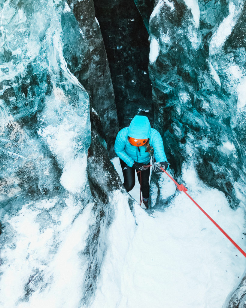 Woman in blue Rab microlight jacket and orange helmet climbing inside Vatnajokull Glacier