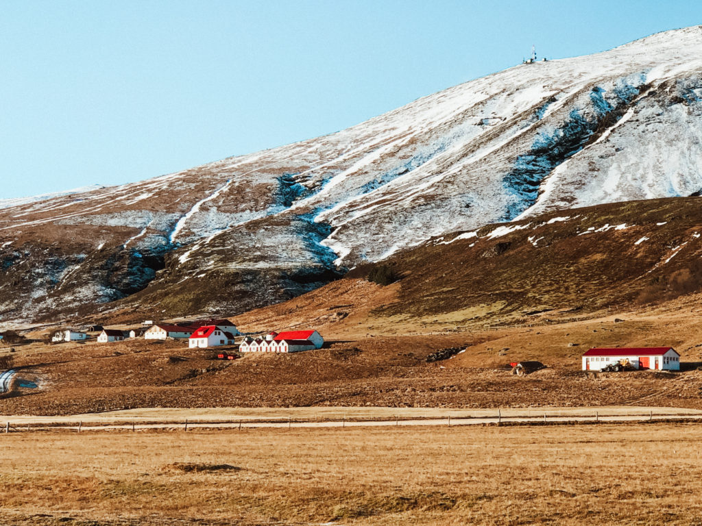 Traditional Icelandic homes with white walls and red roofs at the bottom of a snow covered mountainside