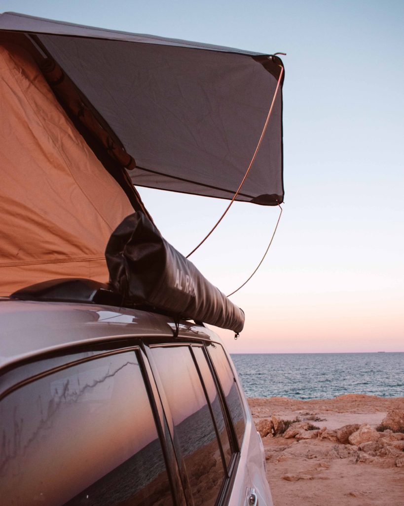 Sunset reflected in car windows under a roof tent near Fins Beach, Oman