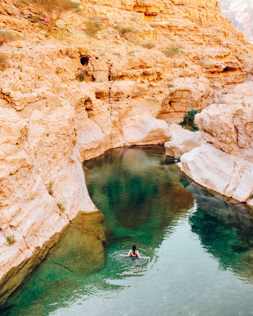 Woman in green pool in Wadi Shab surrounded by rocky gorge