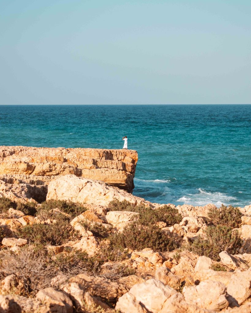 Omani man in white dish dash standing the cliffs at Fins Beach