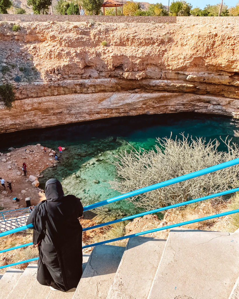 Omani lady in a black abaya standing above the green waters of Bimmah Sinkhole