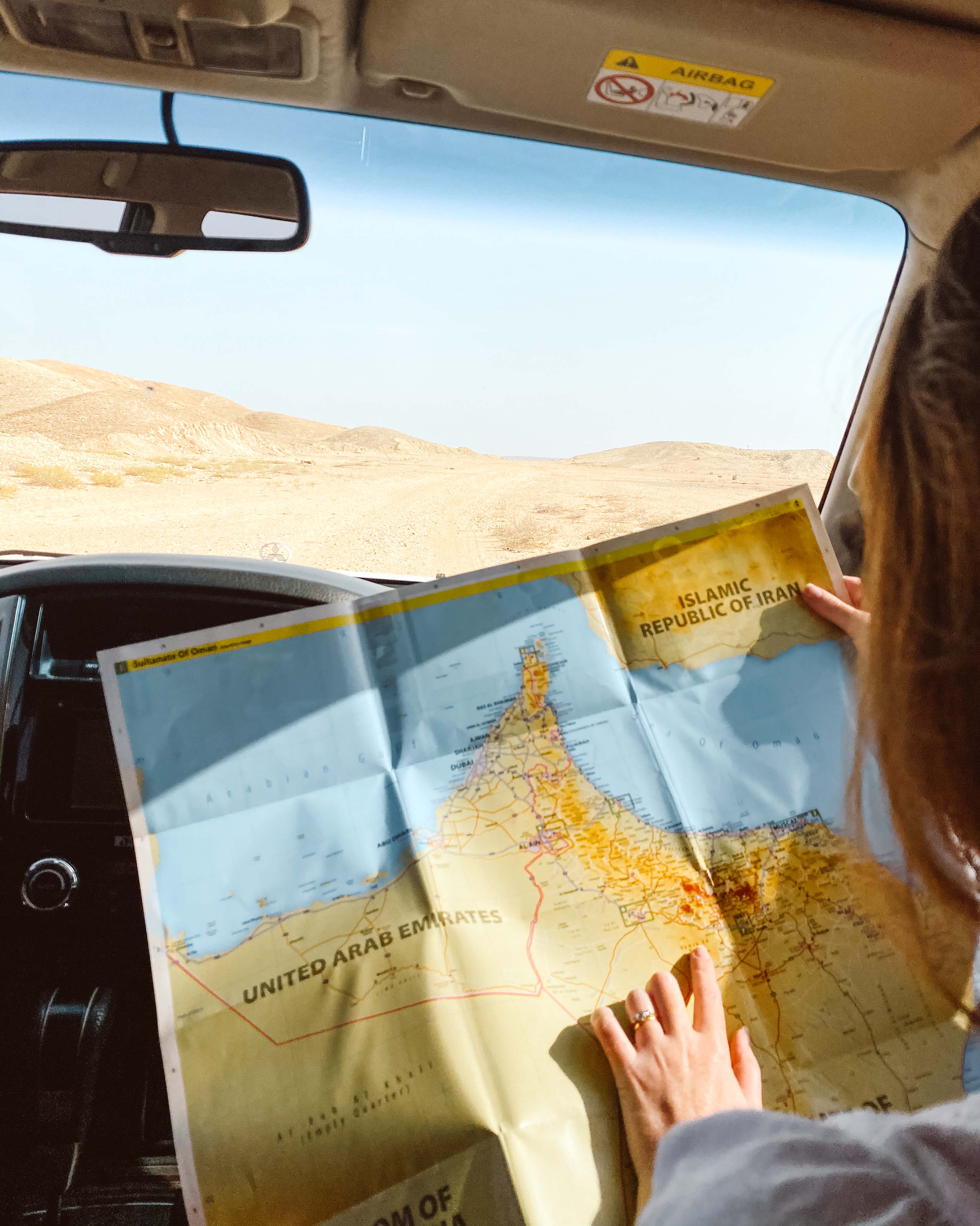 Woman looking at a map of Oman in the front of a car