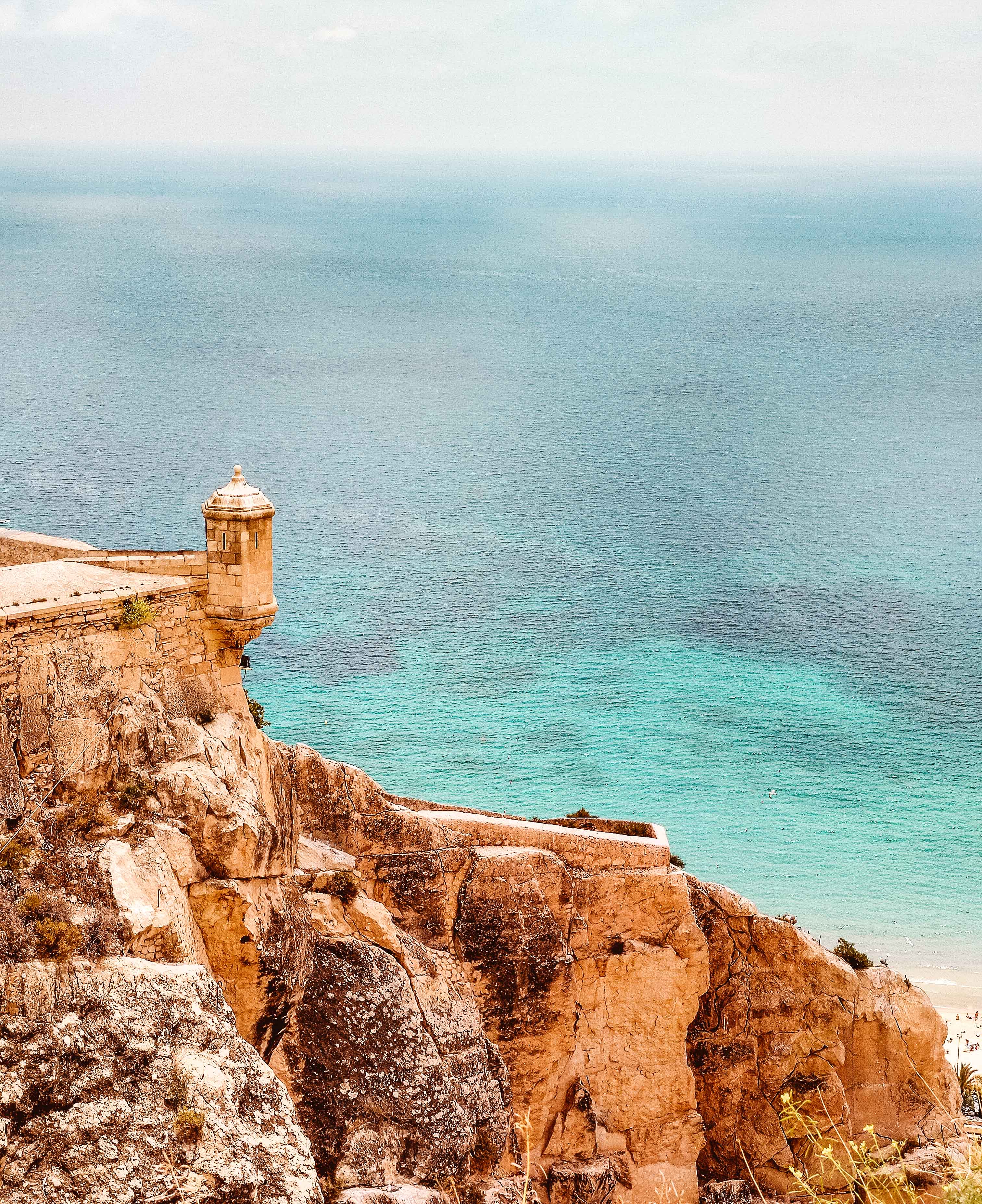 Stone tower of Castillo de Santa Barbara in front of turquoise sea.