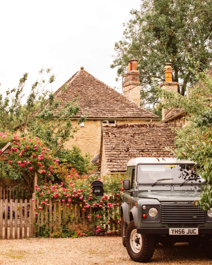 Green landcover parked in front of Cotswolds honey coloured stone houses and pink roses.