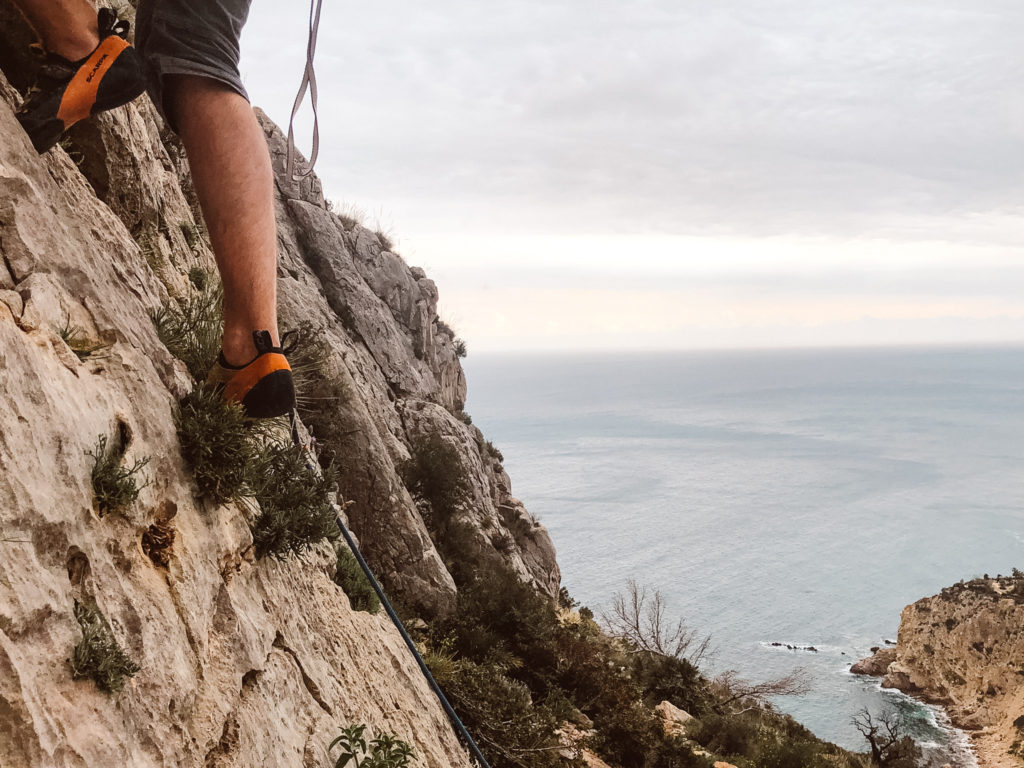 Man's feet rock climbing above the sea at Sierra de Toix.