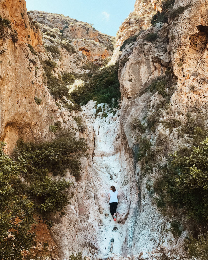 Woman climbing up rock to get to Cala des Testos. 