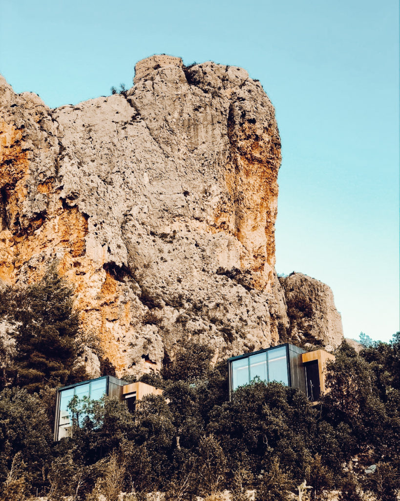 Cube rooms of the VIVOOD Landscape Hotel nestled into the trees beneath large rock face. 