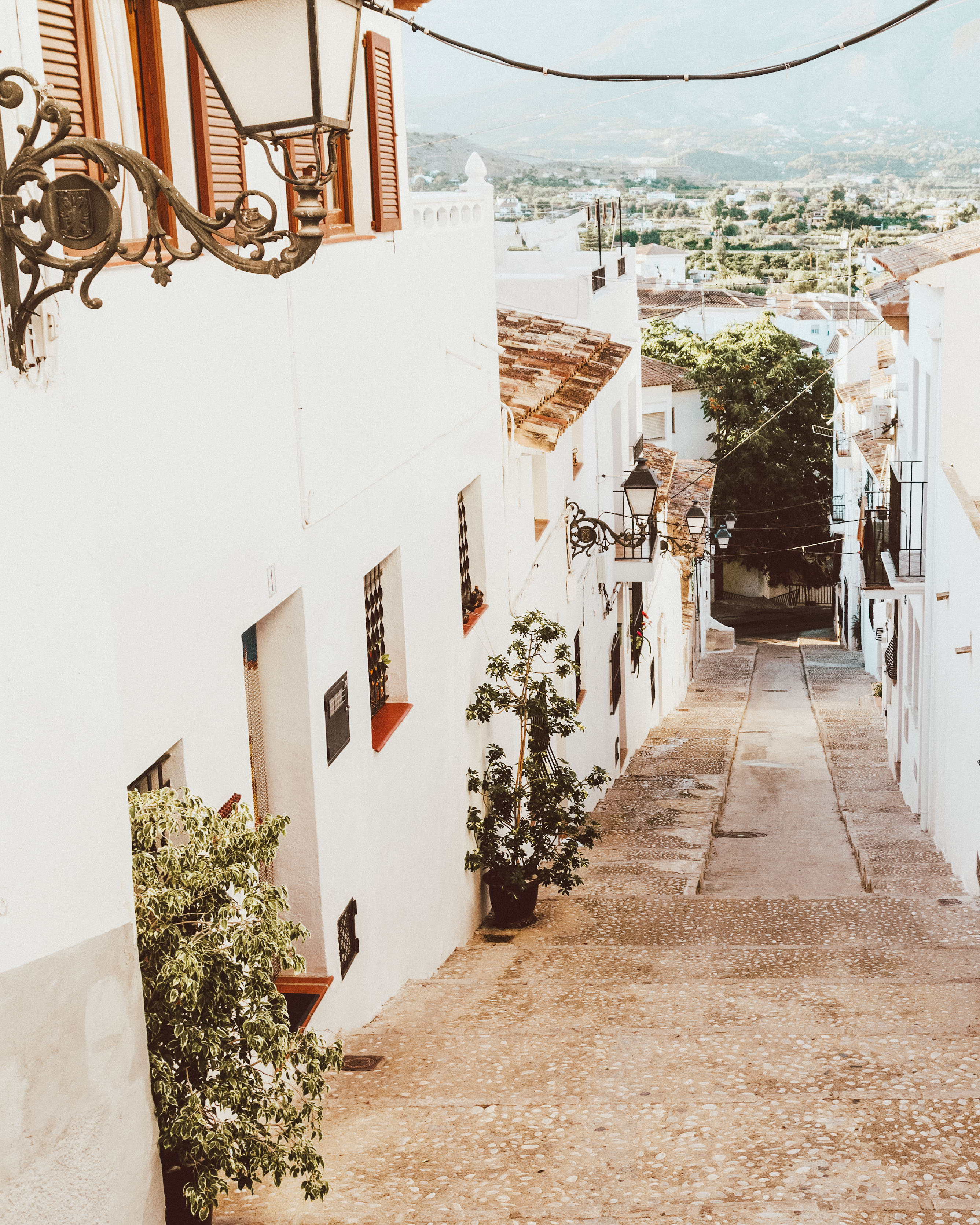 Narrow white streets of Altea looking out over green trees. 