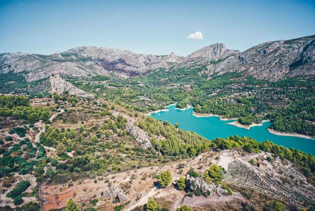Emerald green Guadalest Reservoir amongst green shrubby hillsides. 