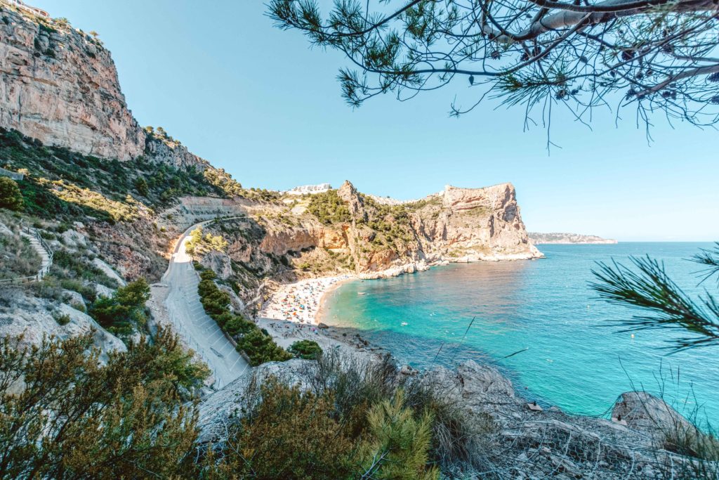 Blue swathe of sea at Cala del Moraig in front of green scrubby rocks. 