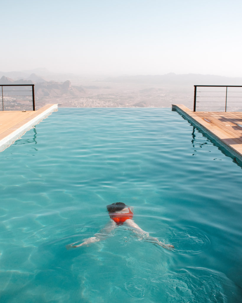 Woman in bright red swimming costume swimming in an infinity pool in Oman's Hajar Mountains