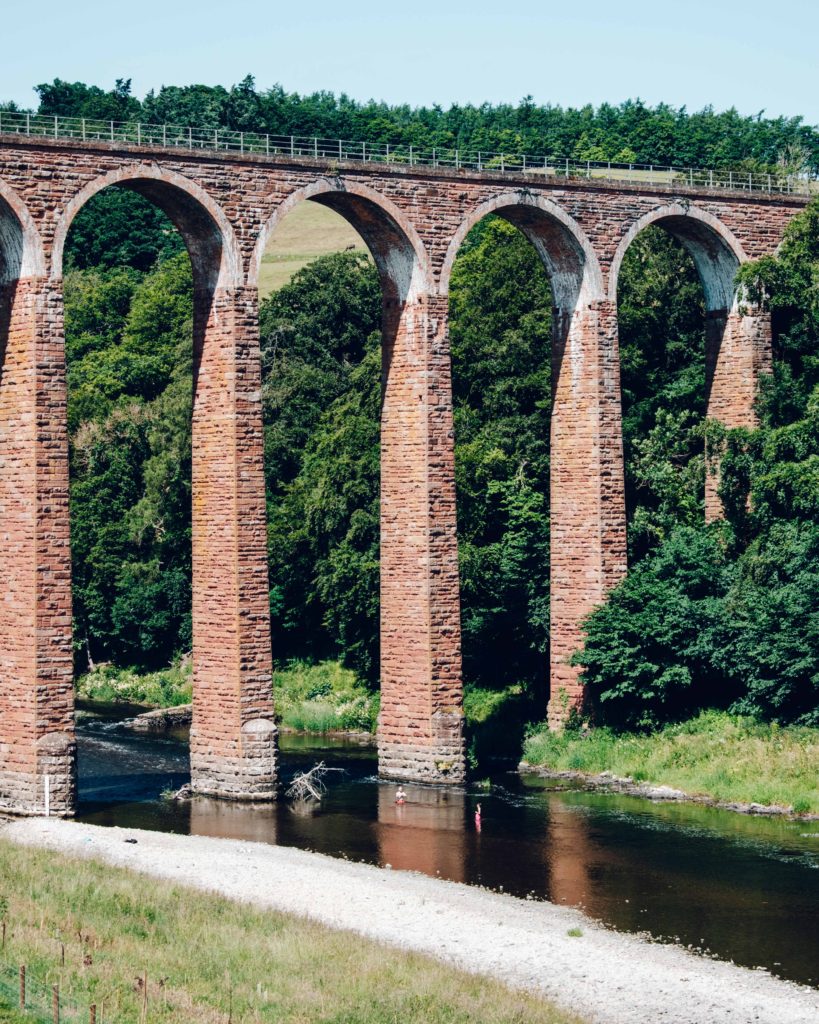 Couple in bright swimming costumes swimming under the Leaderfoot Viaduct in the River Tweed