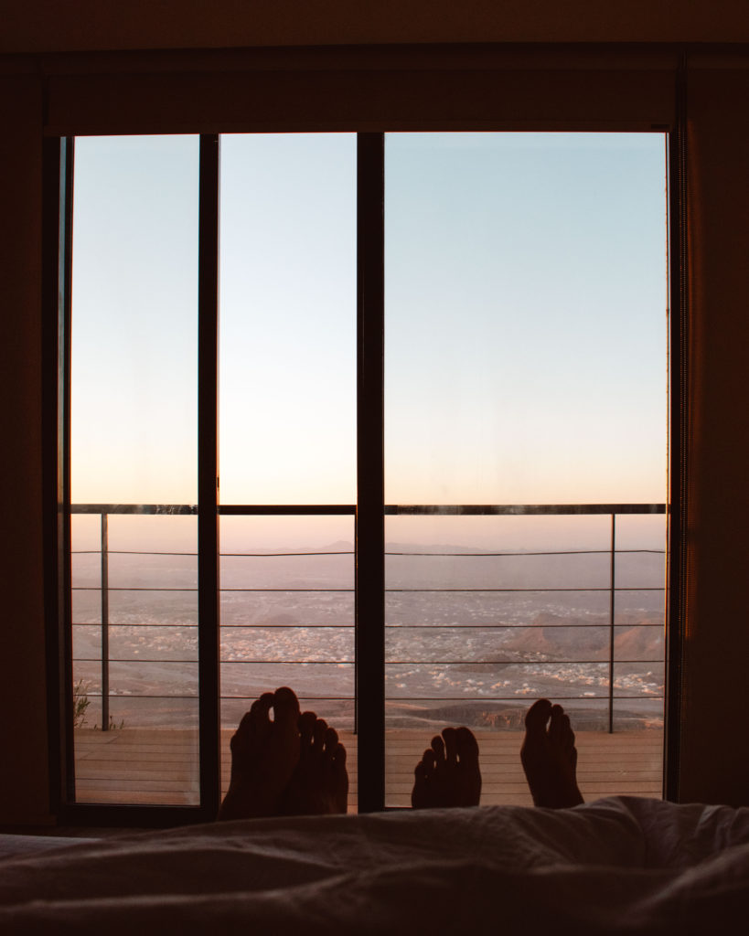 Two pairs of feet in bed with a view of sunrise over Al Hamra