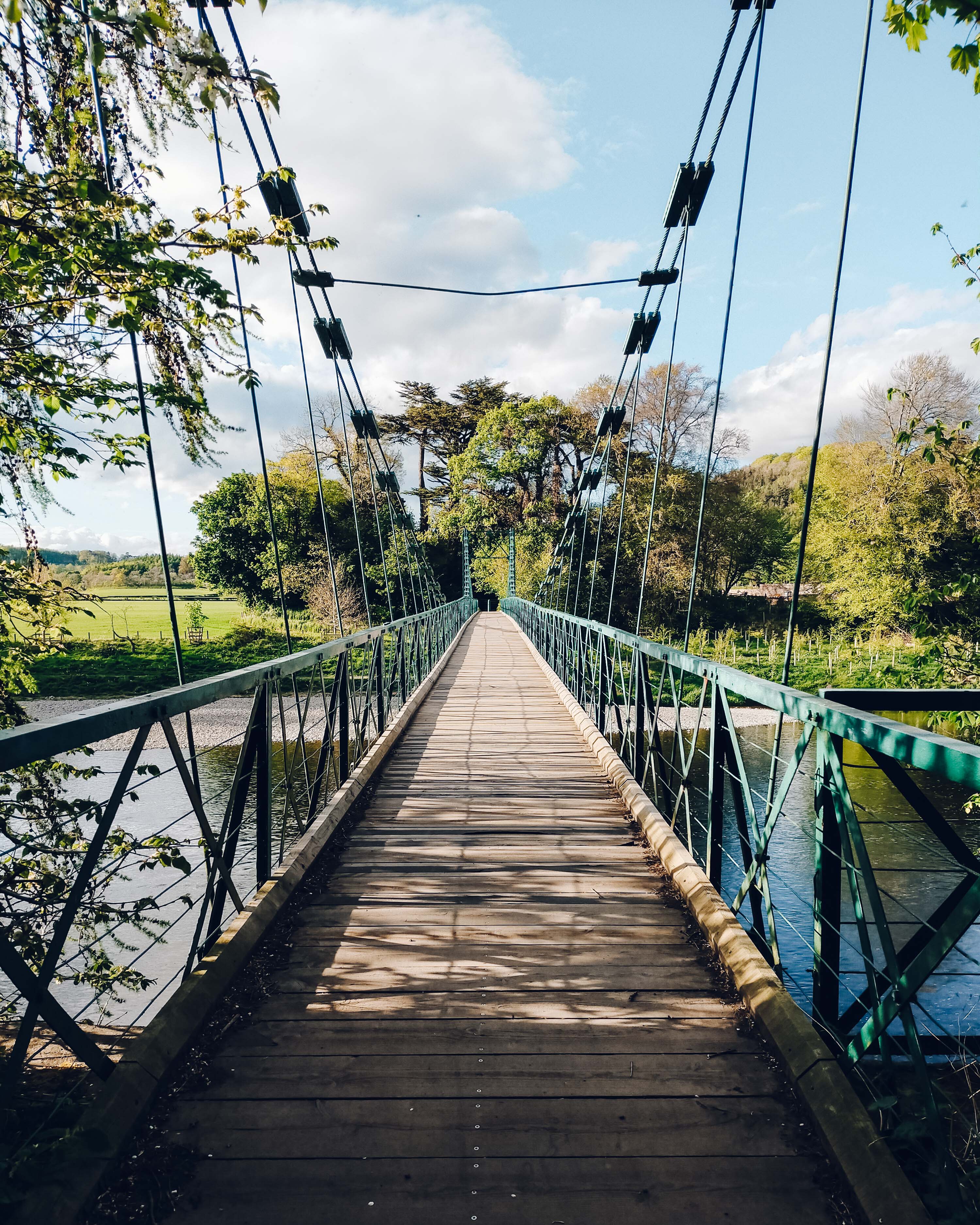 View looking down the Dryburgh Suspension bridge on a green sunny day