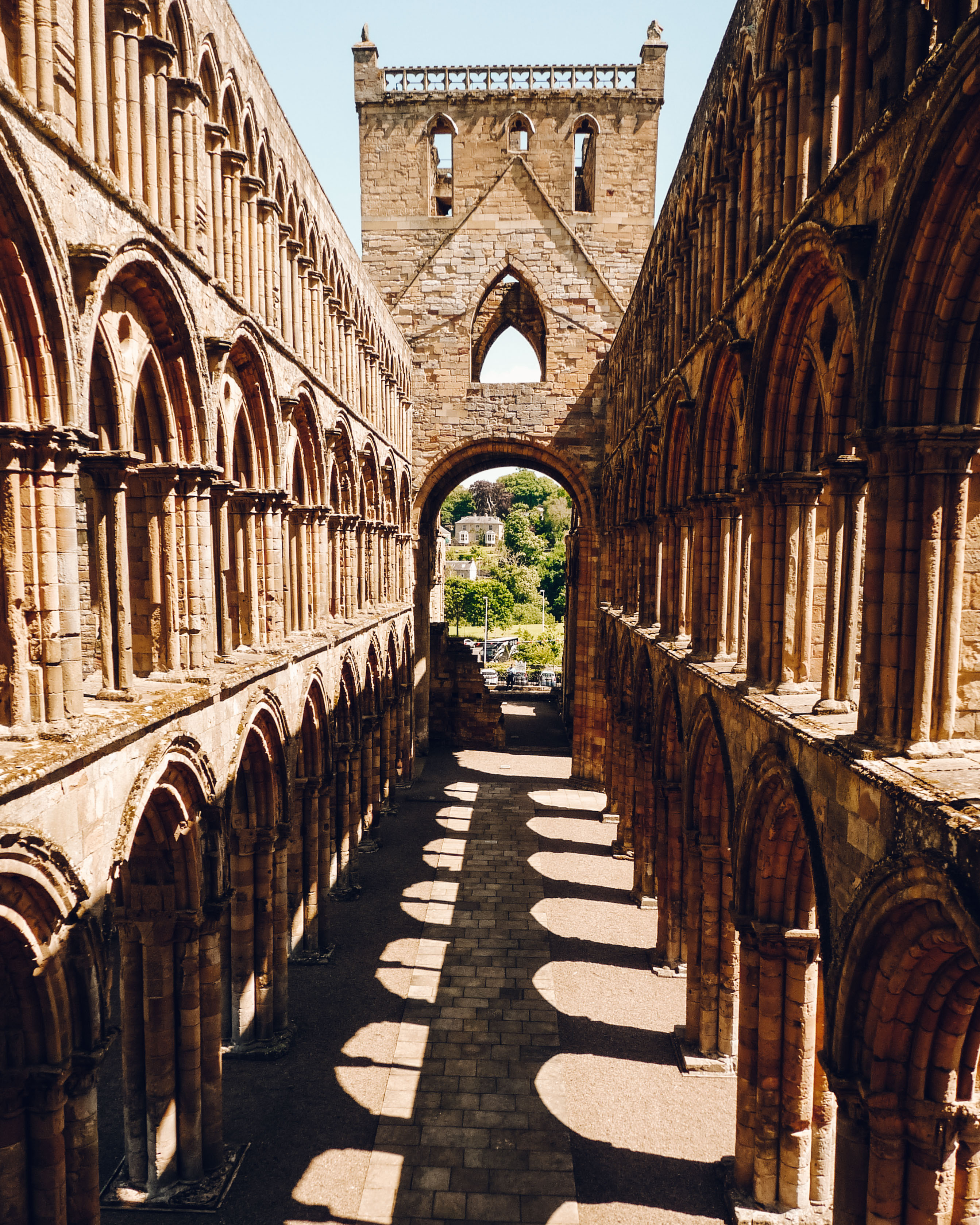 View down the middle of the ruined Jedburgh Abbey with two storey of stone arches and trees beyond