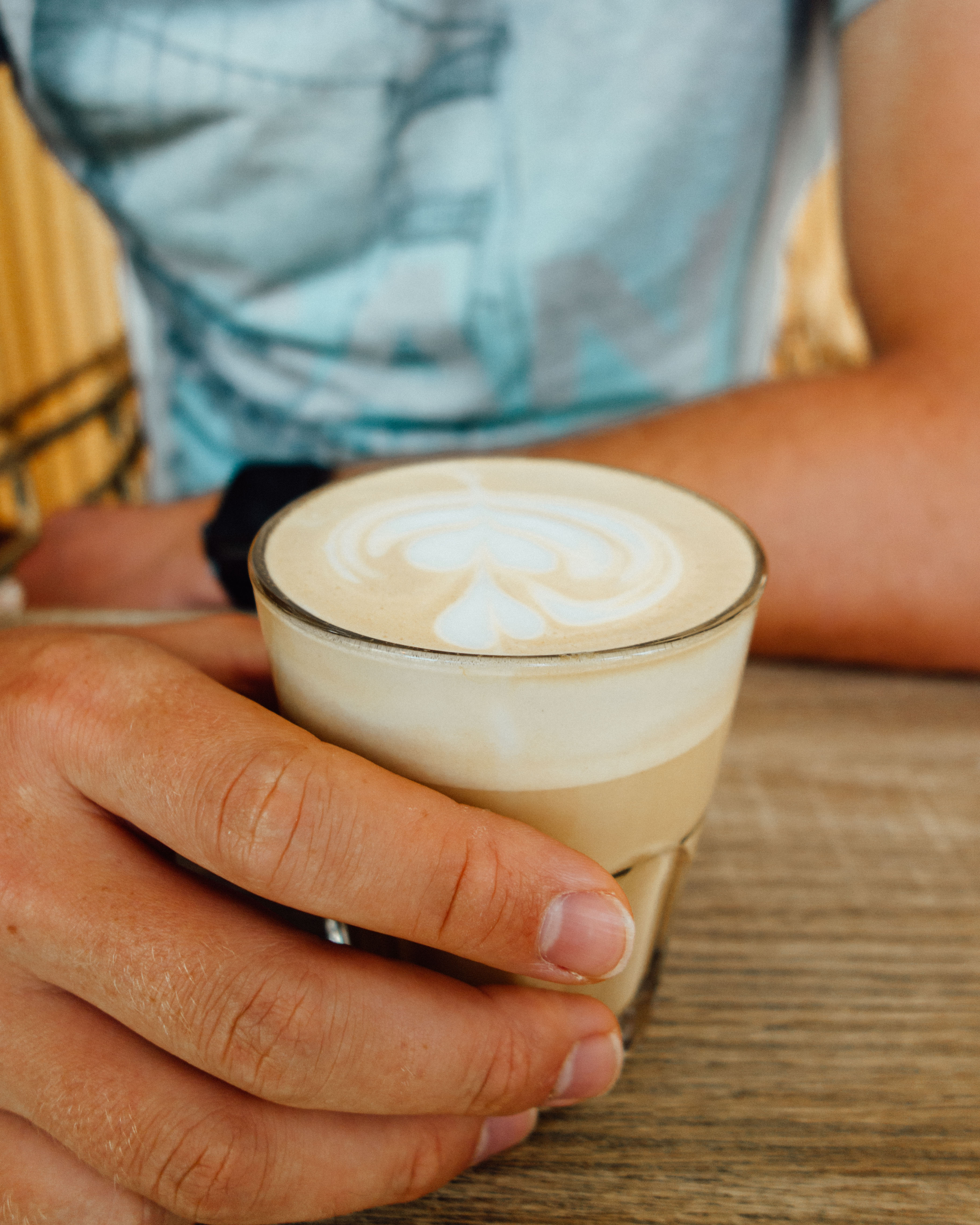 Man in blue t-shirt holding a glass cup of coffee at The Courtyard by M&C, Muscat