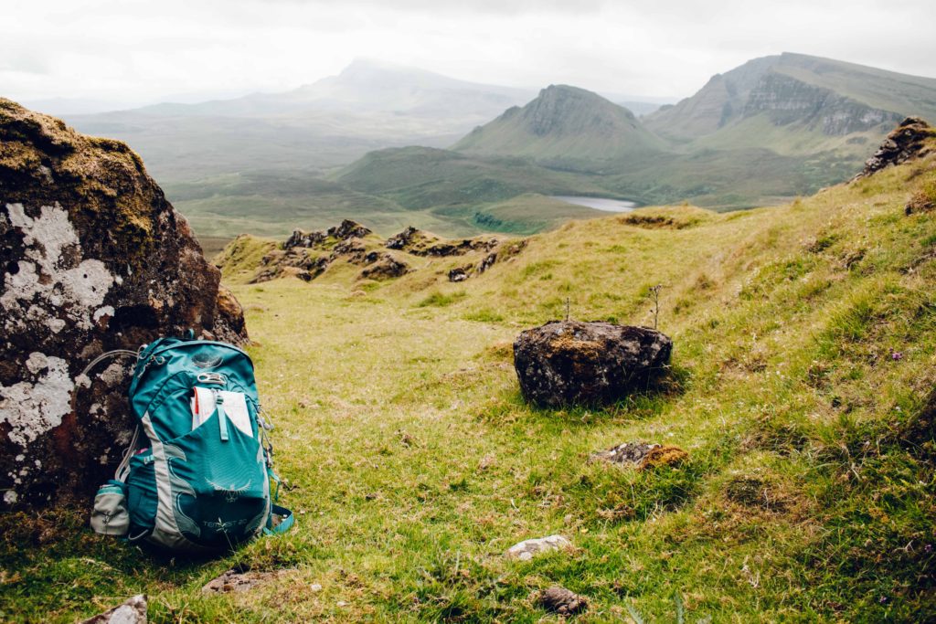 Green Osprey rucksack resting against a large rock in front of rugged green mountains on a misty day at the Quiraing on Skye