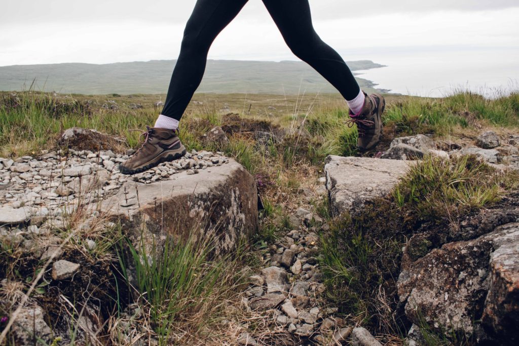 Woman in hiking boots jumping between two rocks whilst walking up Coire Lagan
