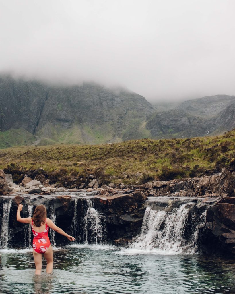 Woman in red and pink swimming costume wading through water at the Fairy Pools on Skye