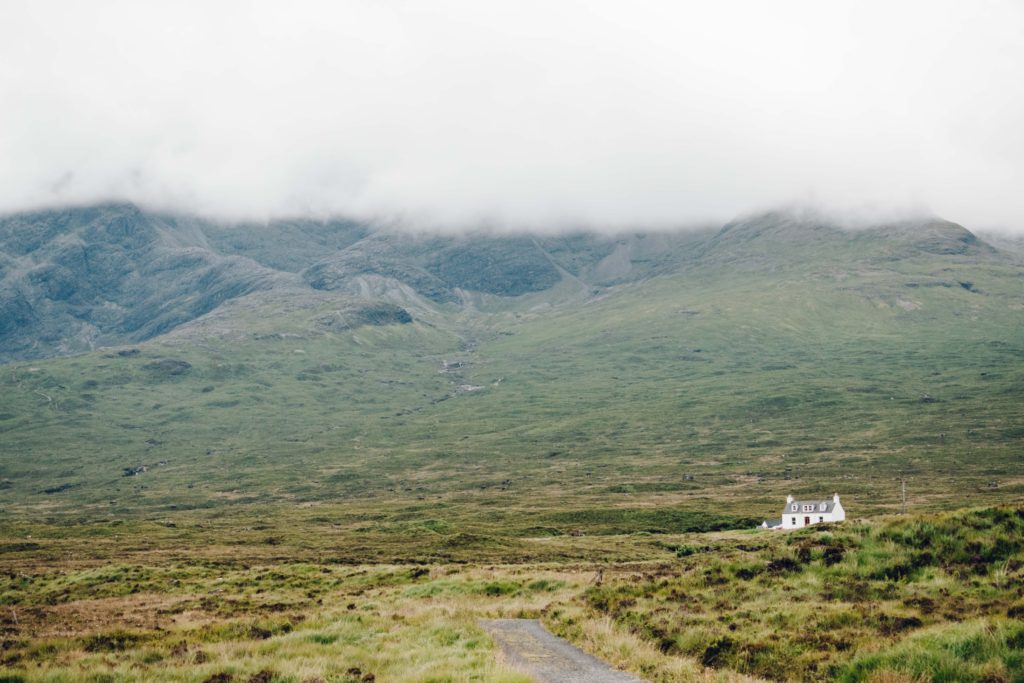 Small white stone house under cloud covered mountains on the Isle of Skye